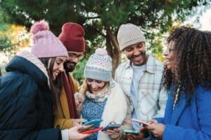 Group of multiracial young friends with coats and hats smiling and watching the social media with a